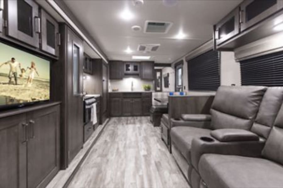 Spacious RV rental interior featuring a modern living area, kitchen, and comfortable gray recliners.