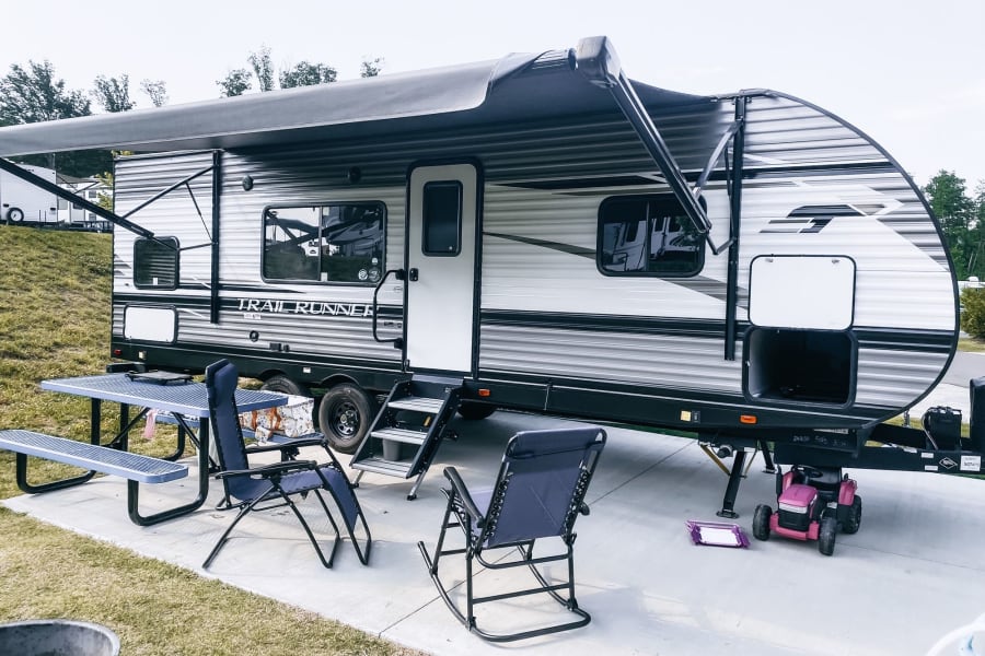 Enjoying an RV rental setup: a large travel trailer with awning, picnic table, chairs, and a child's toy tractor at a campsite.