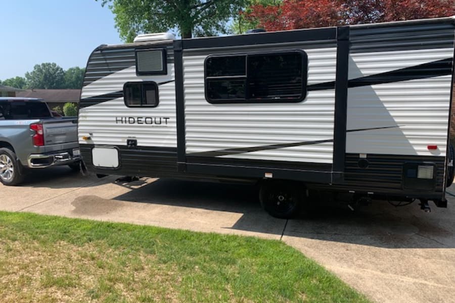 RV rental ready: A grey pickup truck is hitched to a white & black Hideout travel trailer on a sunny driveway.