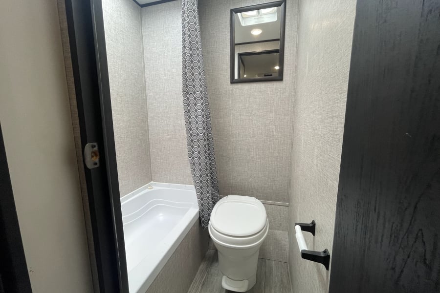 Explore this practical RV rental bathroom featuring a compact tub, toilet, and modern grey interior for your travels.