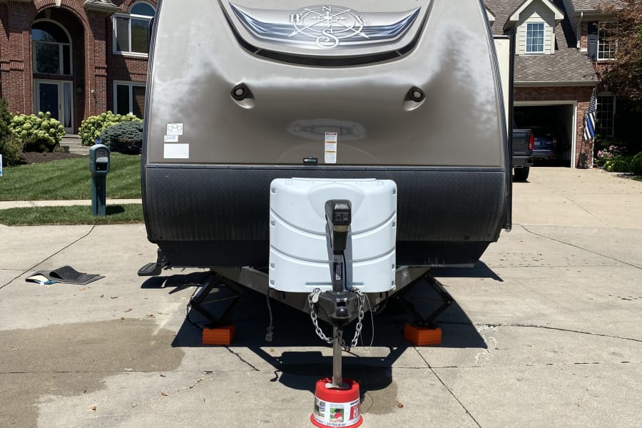 Full front view of a tan "Surveyor by Forest River" travel trailer parked in a driveway, ready for an RV rental getaway!