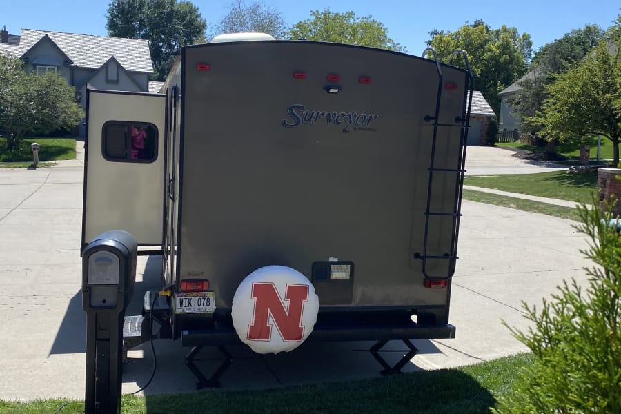 Surveyor travel trailer RV rental, with Nebraska 'N' tire cover, parked on a sunny driveway, ready for adventure.