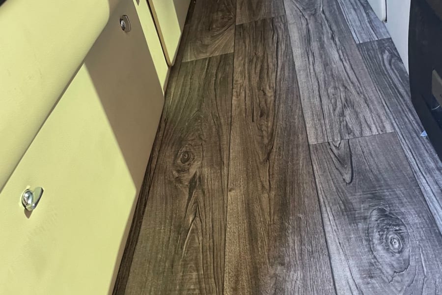 RV rental interior featuring a gray wood-look floor and light beige bench seating with storage compartments.