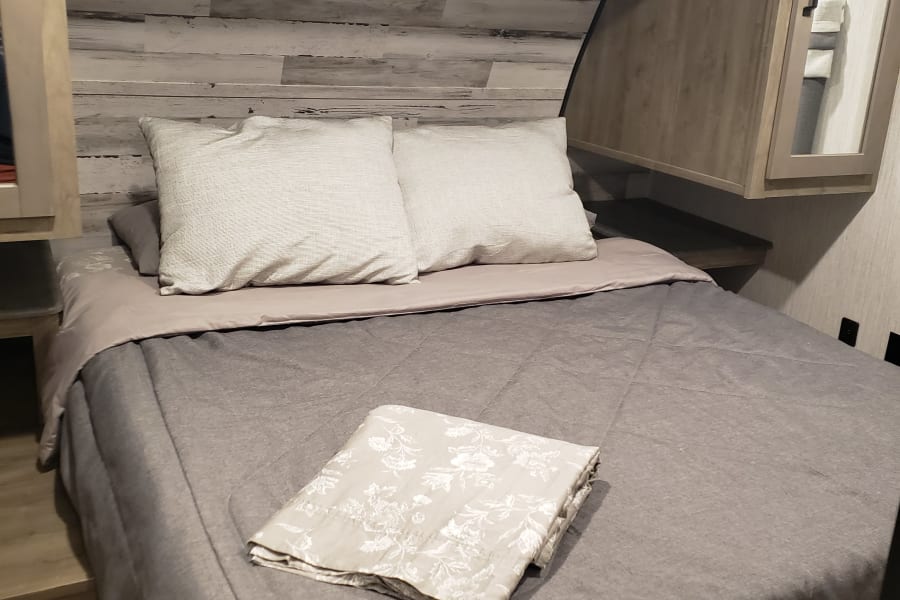 Cozy RV rental bedroom with light wood accents, comfortable bed, and soft gray bedding, ideal for your travels.