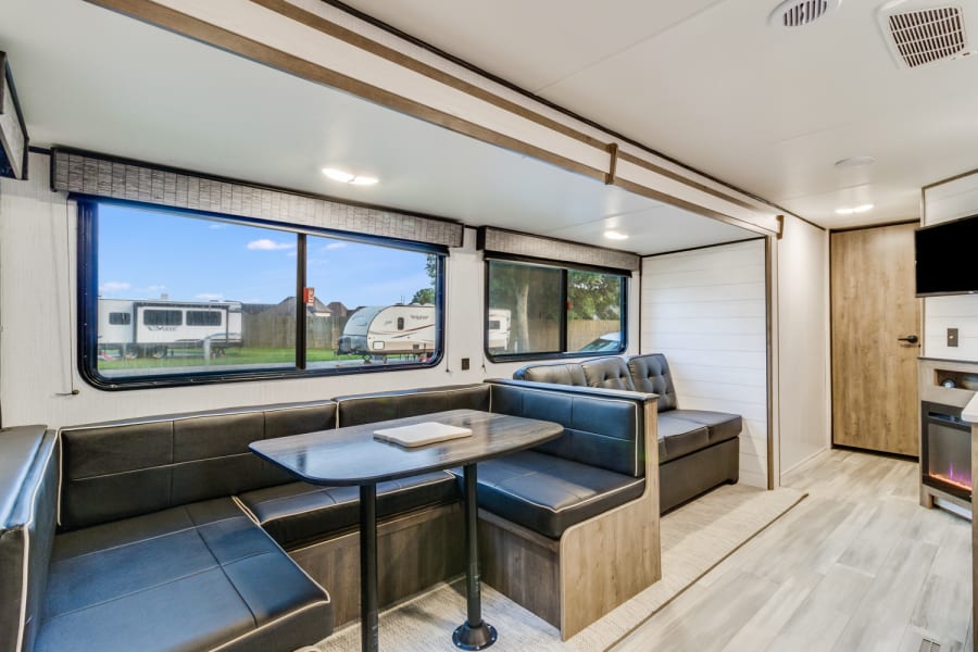 Modern rv rental living space with a dining booth, lounge seating, and entertainment center inside.