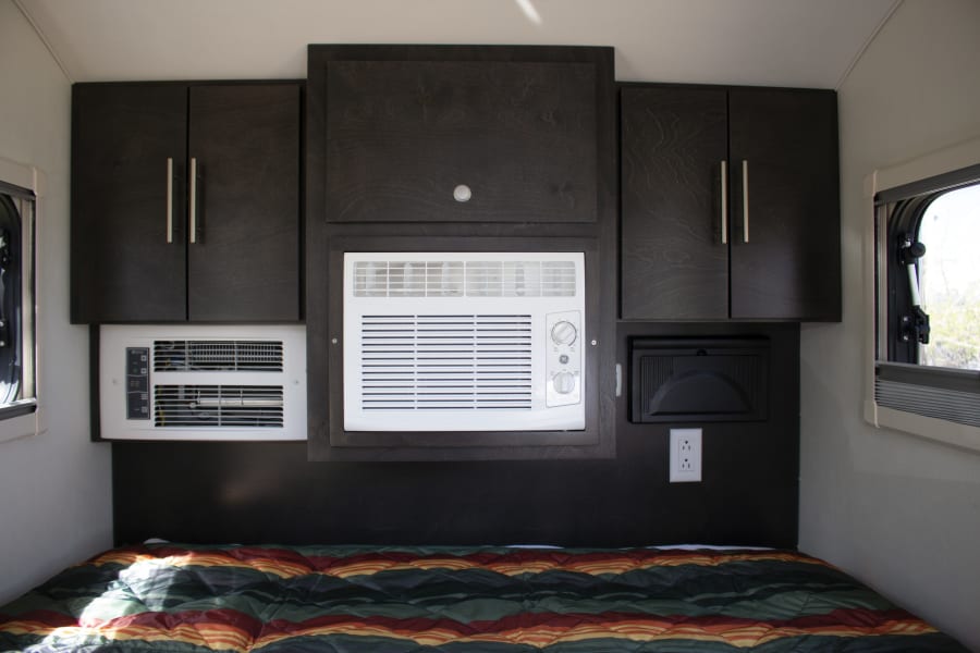 Inside a cozy rv rental: bed, dark cabinets, and dual AC units ensure comfort for travelers.