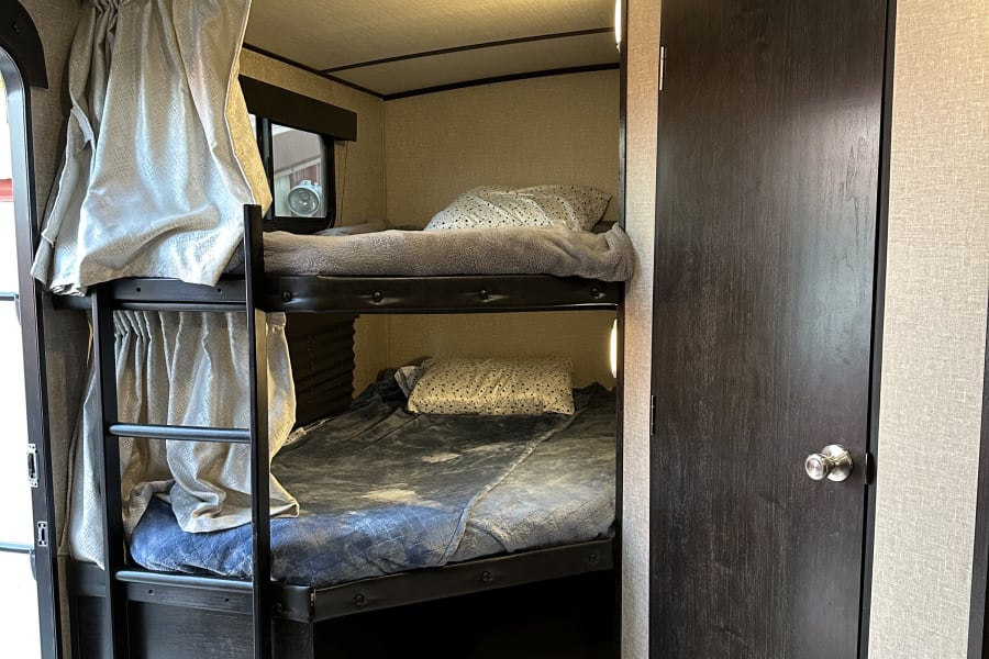Cozy RV rental interior: stacked bunk beds with bedding, privacy curtains, and a dark door. Ideal compact sleeping area.