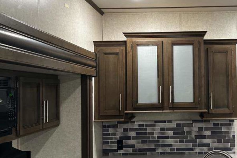 Modern RV rental kitchen with dark cabinets, glass, tiled backsplash, light counters, and sink.