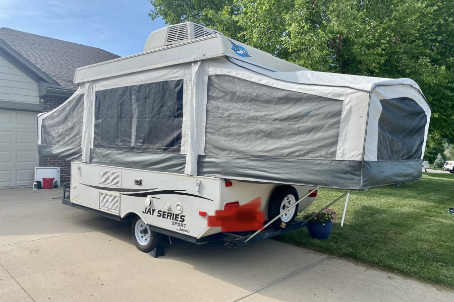 Gray Jayco pop-up camper RV rental fully extended in a driveway on a sunny day.