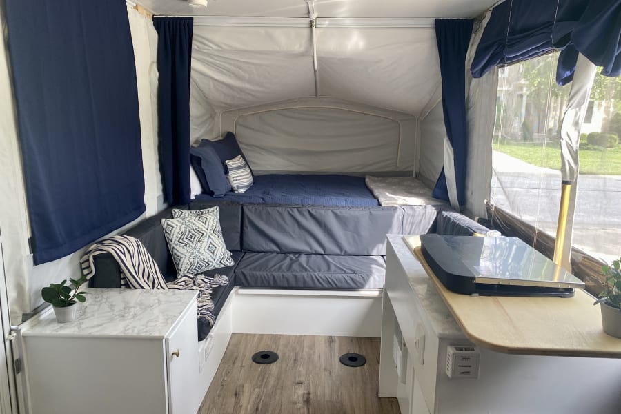 Bright, renovated pop-up camper interior showcasing a bed, L-shaped lounge, and kitchen counter for your RV rental trips.