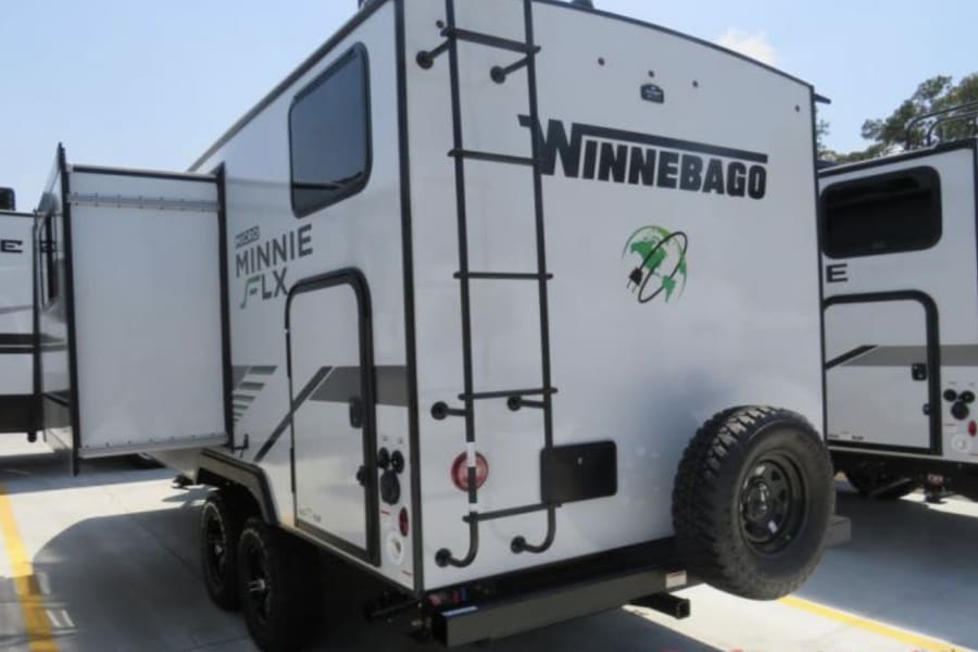 Winnebago Micro Minnie FLX travel trailer, a compact RV rental with a rear ladder, spare tire, and expandable side. Ready for adventure.
