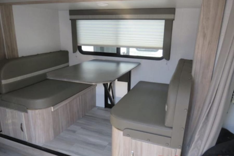 RV rental dinette with comfortable booth seating, a table, and a window with blinds, ideal for meals or relaxation.