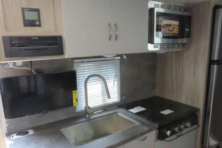 RV rental kitchen: Features a sink, stovetop, microwave, fridge, and TV for comfortable travel.