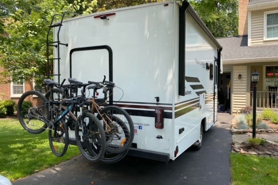 White RV rental with a rear bike rack holding multiple bicycles, parked in a driveway. Ready for outdoor adventure.