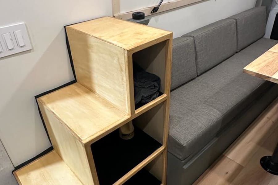 Custom wooden step-shelves and gray bench seating optimize space in this RV rental interior.