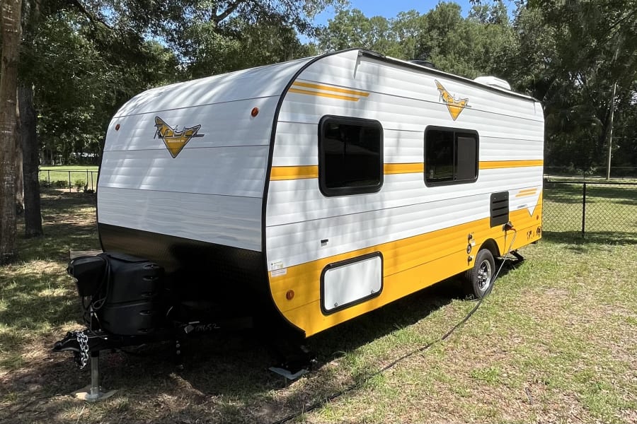 Bright white and yellow travel trailer RV rental parked on a grassy campsite.