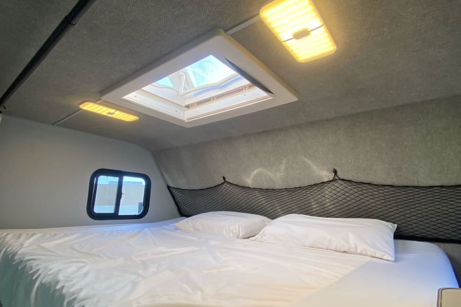 Inside this RV rental: a comfy sleeping area with white bedding, bright LED lights, and a skylight.