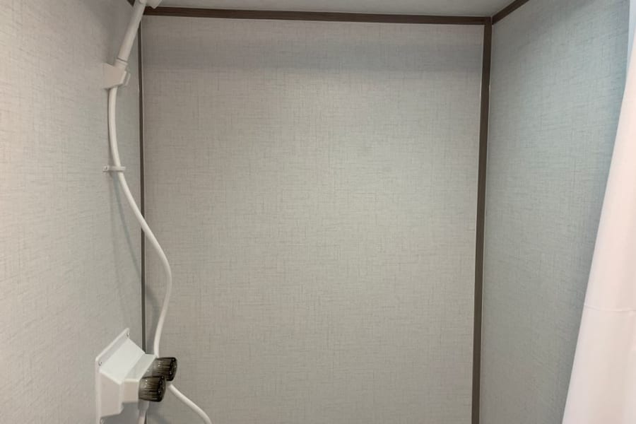 Inside an RV rental: a compact shower with light walls, handheld showerhead, and control knobs for a functional bath.