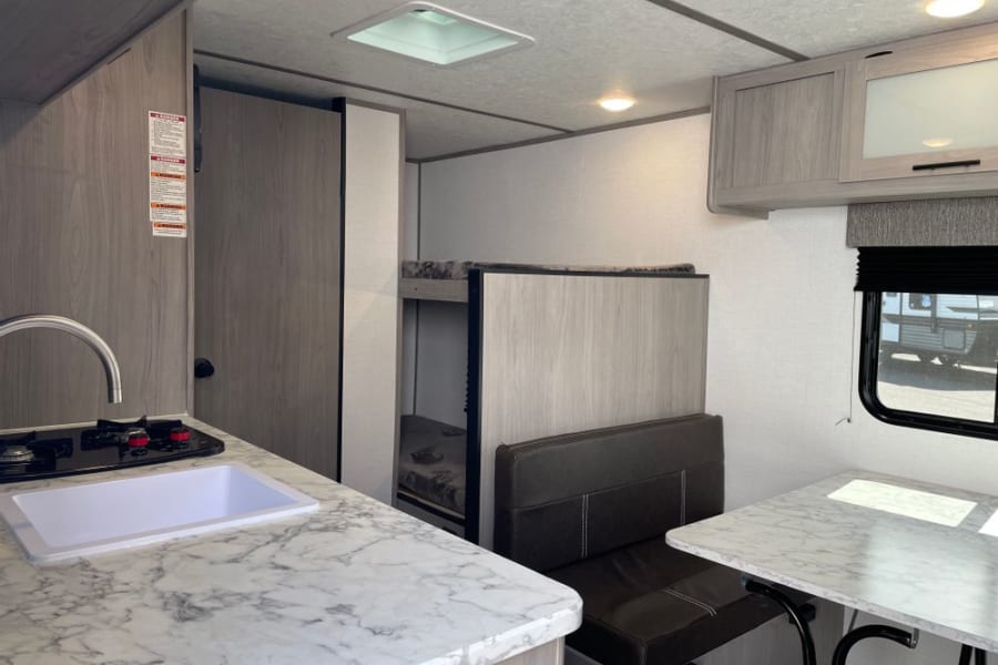 Spacious RV rental interior featuring a modern kitchenette, dining area with seating, and bunk beds. Perfect for family adventures.