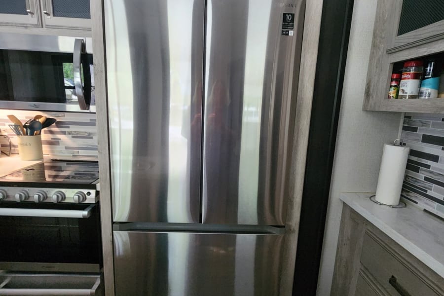 RV rental: modern kitchen with large stainless steel refrigerator, stove, and sleek cabinetry for convenient cooking.