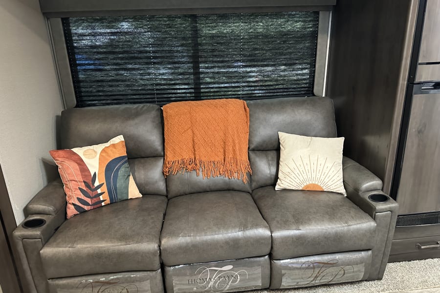Cozy RV rental interior with comfortable reclining sofa, pillows, and throw blanket.