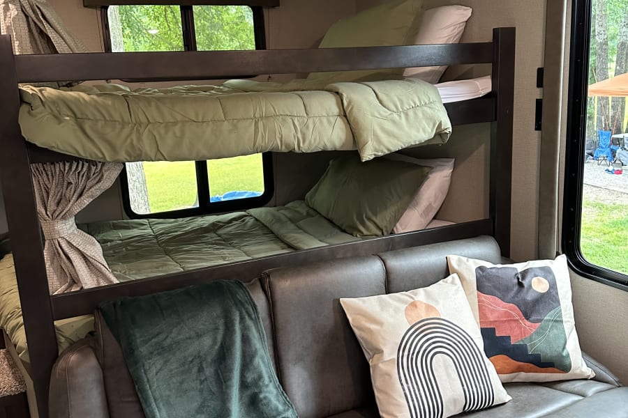 RV rental bunkhouse interior: features cozy bunk beds with green bedding and a comfortable grey sofa with decorative pillows.
