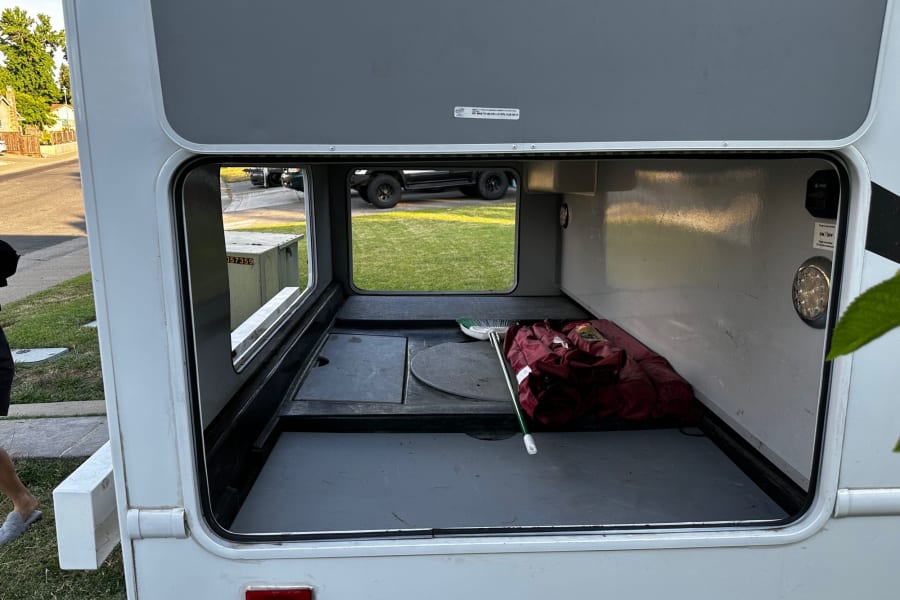 Open RV rental storage: spacious basement with broom, bag, and light. Ready for travel/camping.