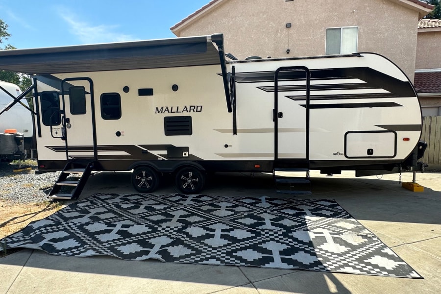 An RV rental travel trailer with extended awning & outdoor mat, parked for leisure. Great for camping.