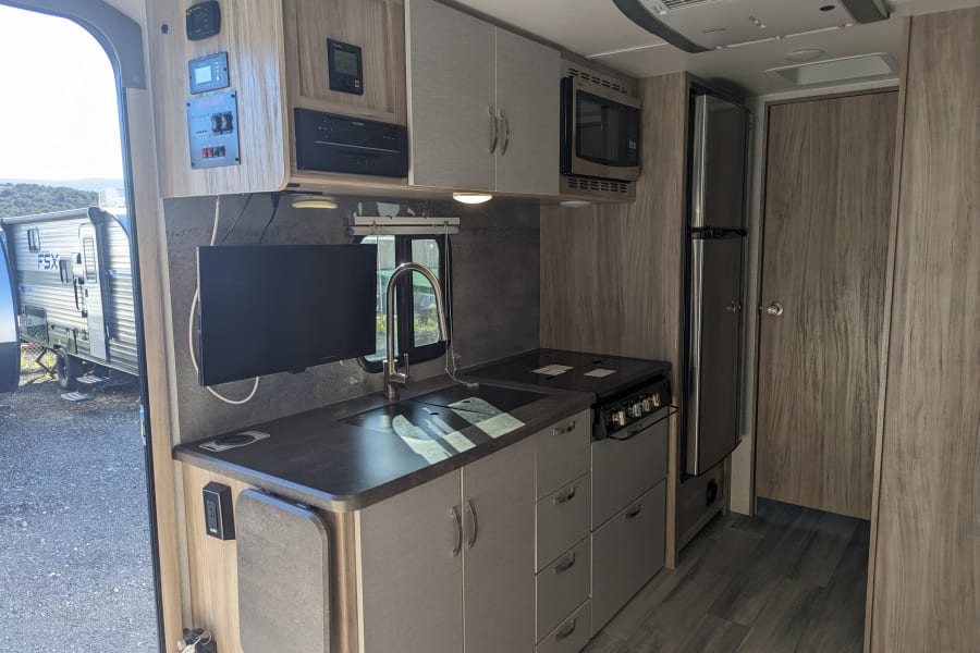 This RV rental offers a well-equipped kitchen area with a sink, stove, microwave, fridge, and entertainment.