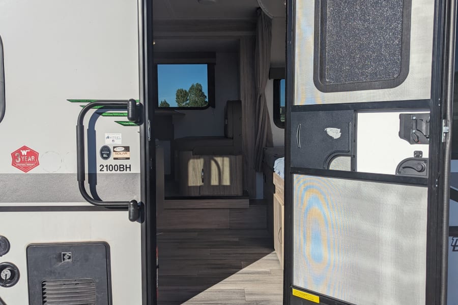 Step into comfort: This rv rental shows its open door revealing a cozy interior, exterior speaker, and convenient entry steps.