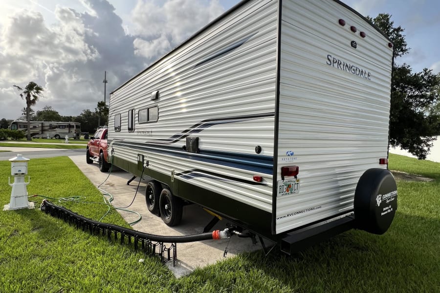 A Springdale RV rental is set up at a Florida campground, featuring a travel trailer with utility hookups on a sunny day.