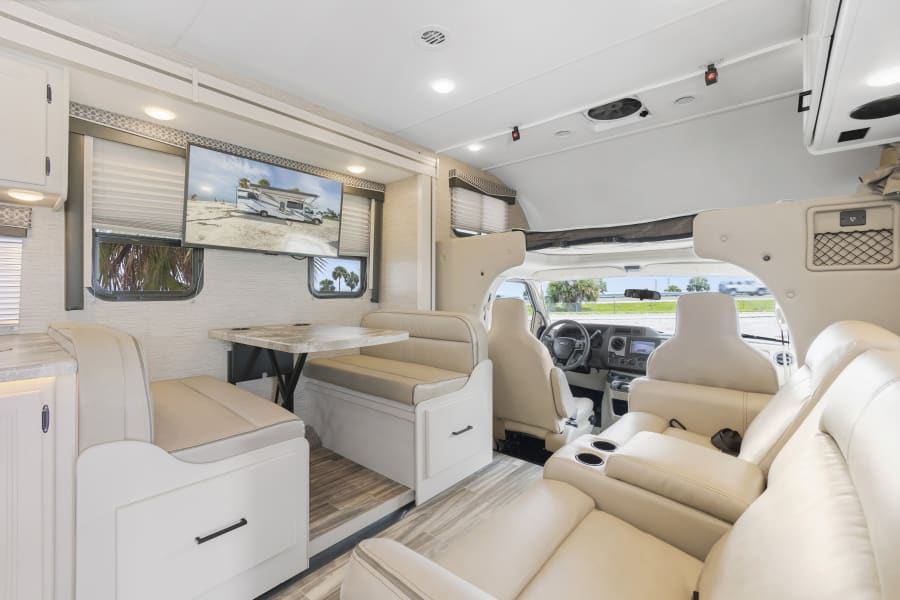 Spacious RV rental interior featuring a bright dinette, mounted TV, and front cockpit. Ideal for comfortable motorhome adventures.
