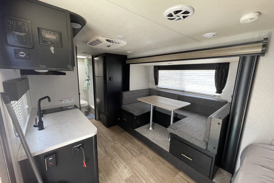 Modern RV rental interior with a functional kitchen, U-shaped dinette, and visible bathroom. Well-appointed for travel.
