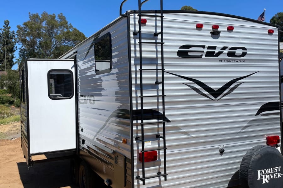 This grey and black Forest River EVO travel trailer, with its slide-out open and rear ladder, is ready for your next RV rental adventure.