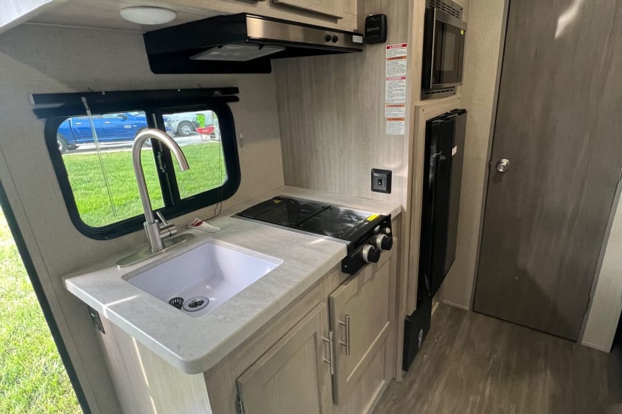 Inside an rv rental: a cozy kitchen area with sink, gas stove, microwave, light wood cabinets & sleek flooring.