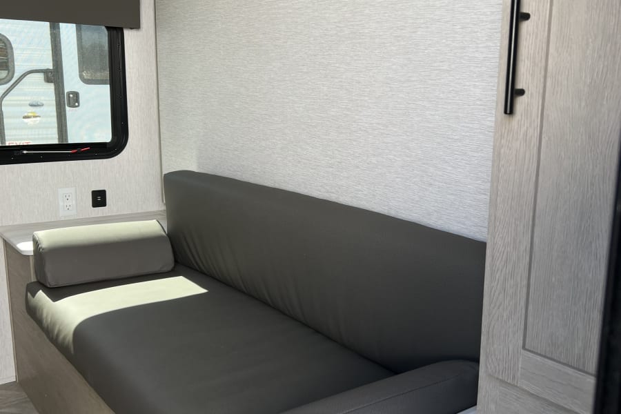 Inside an RV rental: inviting dark gray sofa, light wood cabinetry, and window view, perfect for your next road trip.