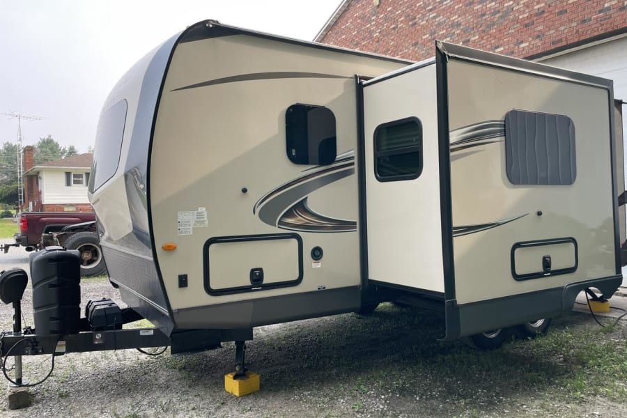 This spacious beige and grey travel trailer RV rental is parked with its slide-out extended, perfect for your next adventure.