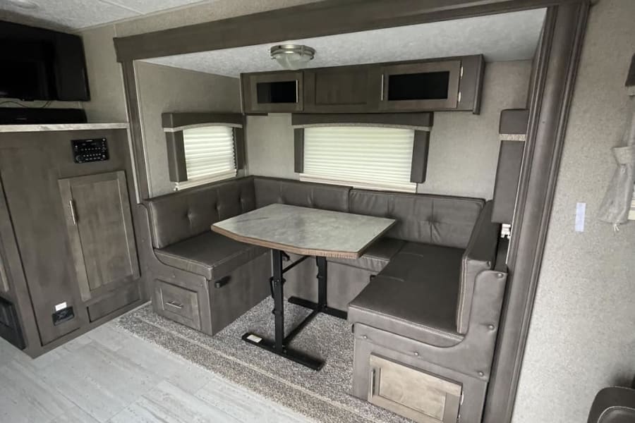 RV rental interior: U-shaped dinette with dark seating, overhead cabinets, and entertainment system.