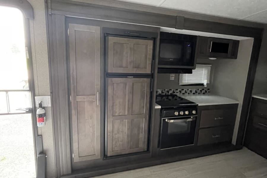 View of an RV rental's compact kitchen, featuring a refrigerator, microwave, and stove/oven, near the entry door.