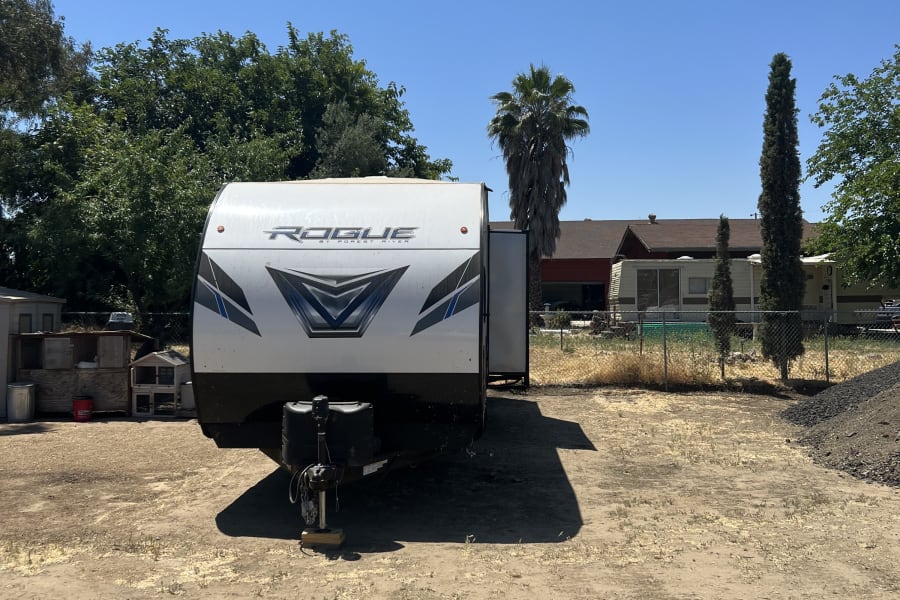 Explore with our RV rental! A bright white travel trailer is parked on a sunlit dirt lot, ready for adventure.