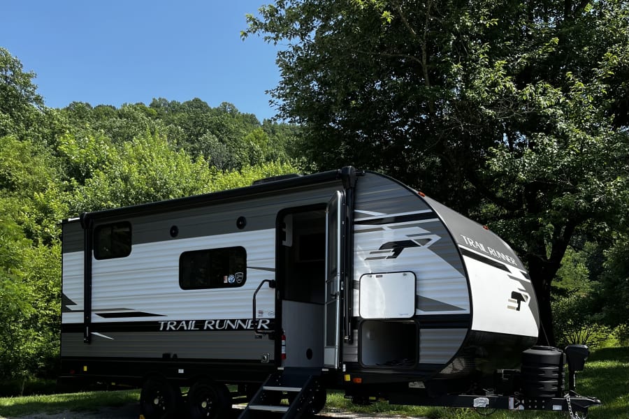 This Trail Runner travel trailer RV rental is perfectly set up at a sunny campsite, ready for your next adventure.