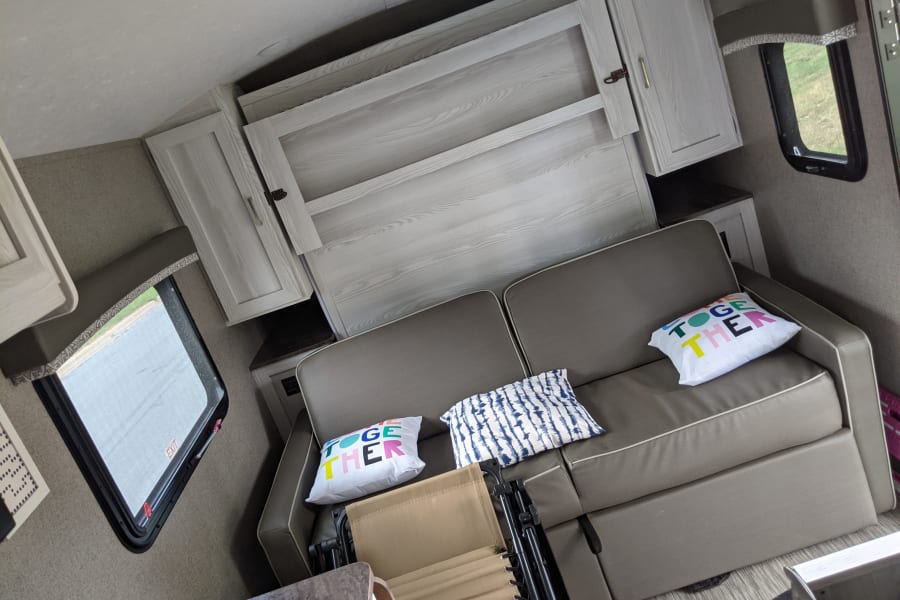 Cozy rv rental living space with a comfy sofa, colorful pillows, and a clever folded Murphy bed.