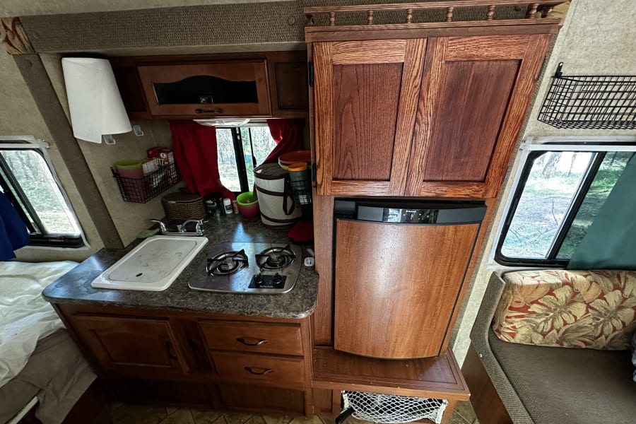 Cozy rv rental interior, showing a compact kitchen with stove, sink, fridge, cabinets, a bed, and seating.