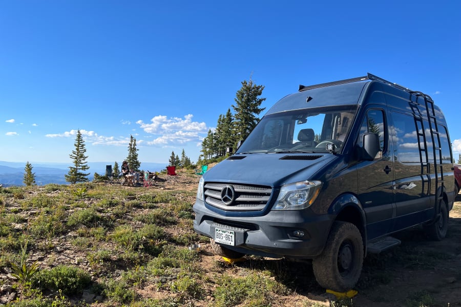 Ultimate RV rental adventure! Blue camper van parked on a mountain overlooking scenic vistas for off-grid camping.