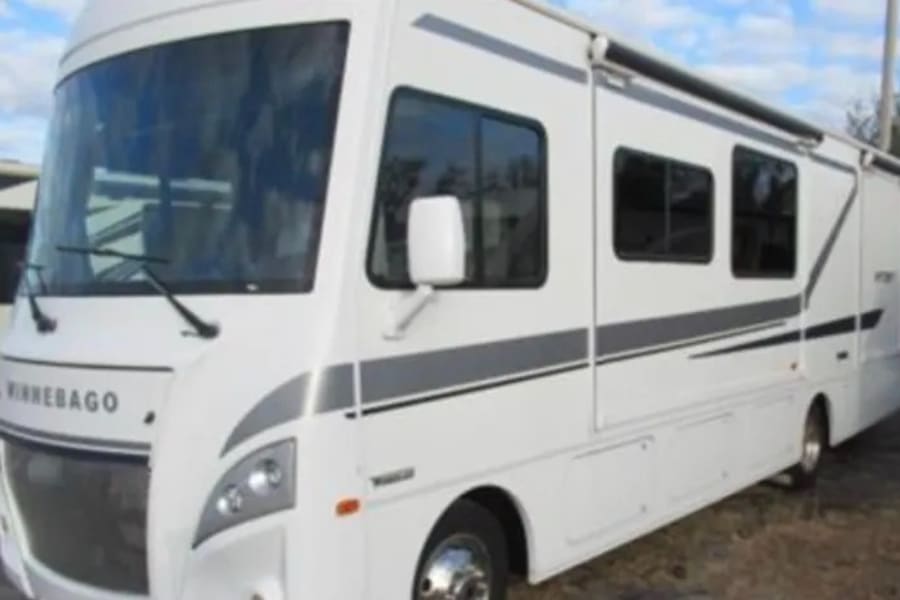 White Winnebago motorhome, an ideal RV rental. Features large windows & an awning for comfortable travel.