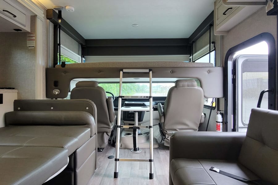 RV rental interior: A cozy cab-over bunk with ladder, spacious dinette/sofa, and driver's area. Modern and ready for travel!