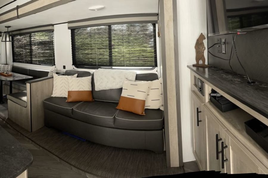Spacious rv rental interior: A modern kitchen, cozy dining booth, comfy sofa, and entertainment center with TV.
