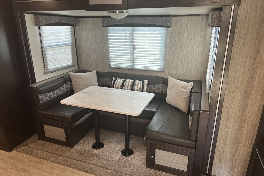 RV rental interior featuring a cozy U-shaped dinette with table and windows, perfect for dining & relaxing.