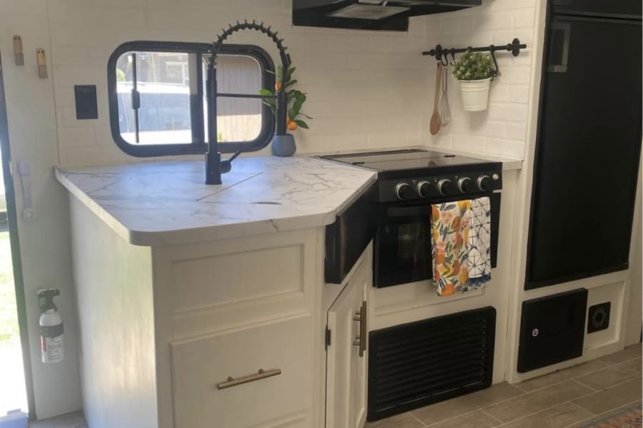 Step inside this modern RV rental kitchen. Features white cabinets, black appliances, marble-look counters, & subway tile backsplash.