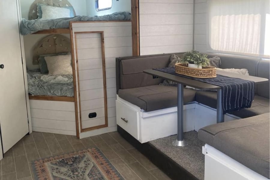 Inside a modern RV rental: built-in bunk beds, U-shaped dinette, and chic wood accents. Comfortable travel awaits!